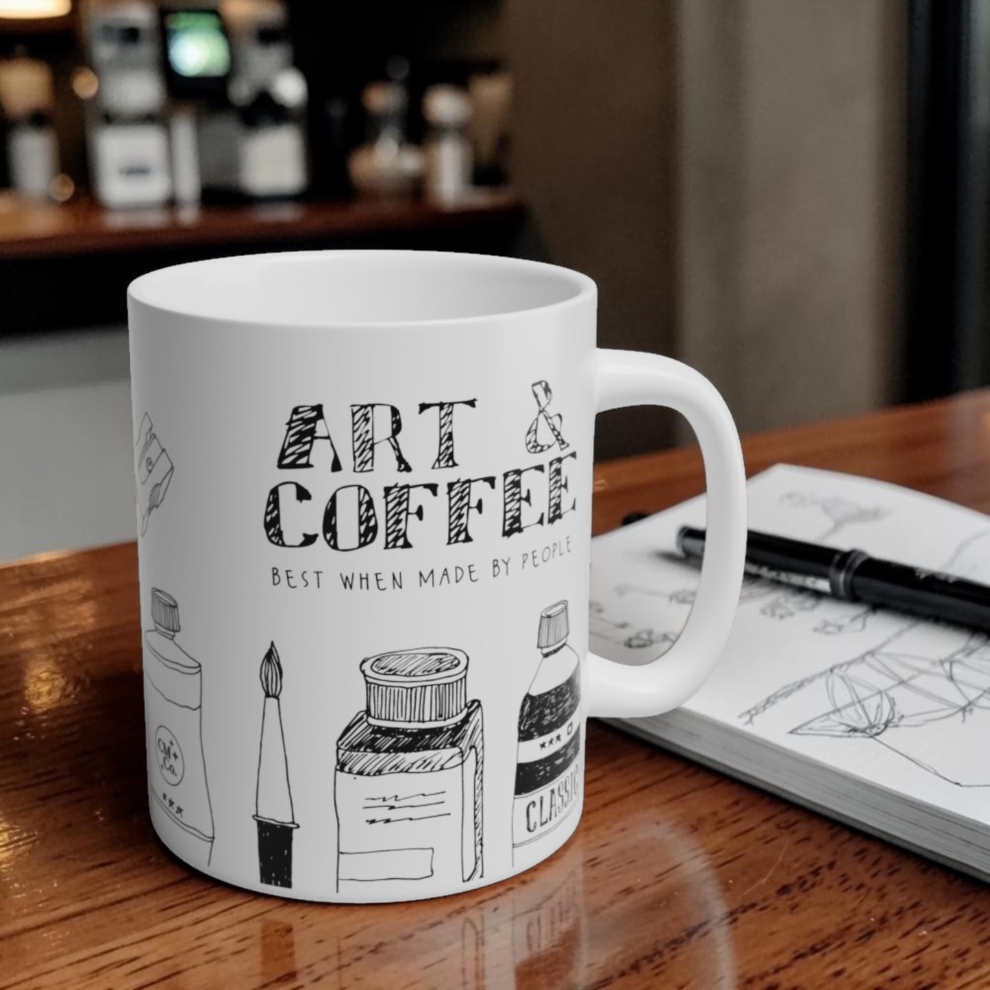White mug with 'Art & Coffee' design on a wooden table with a blurred coffee shop background