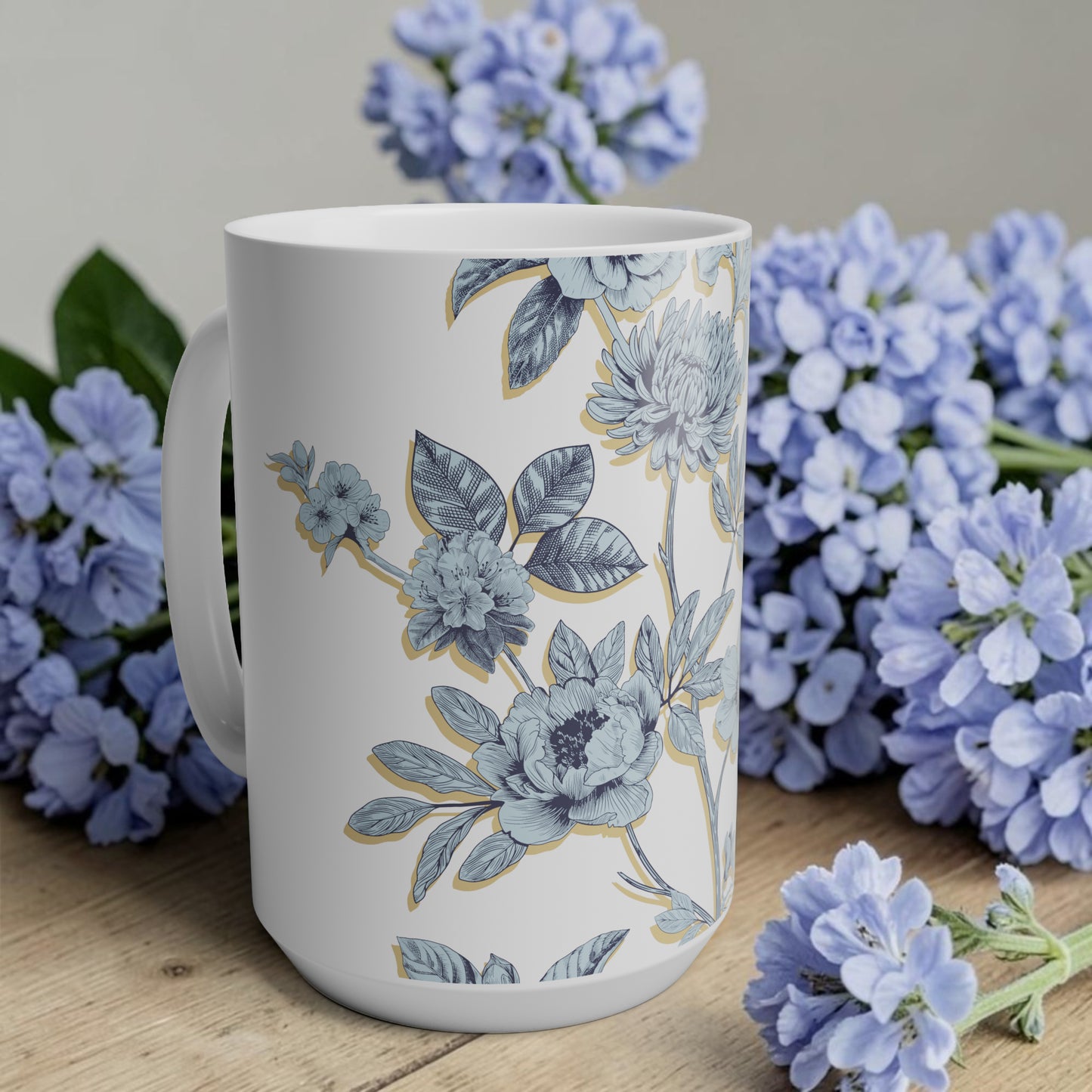 White mug with floral design surrounded by blue flowers on a wooden surface