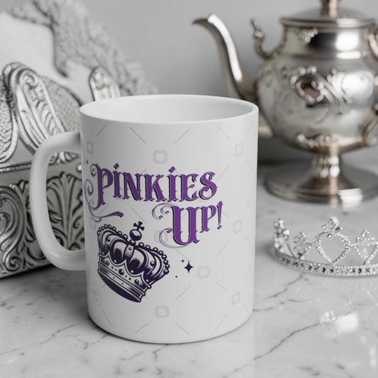 White mug with purple text 'PINKIES UP!' on a marble surface with decorative items.