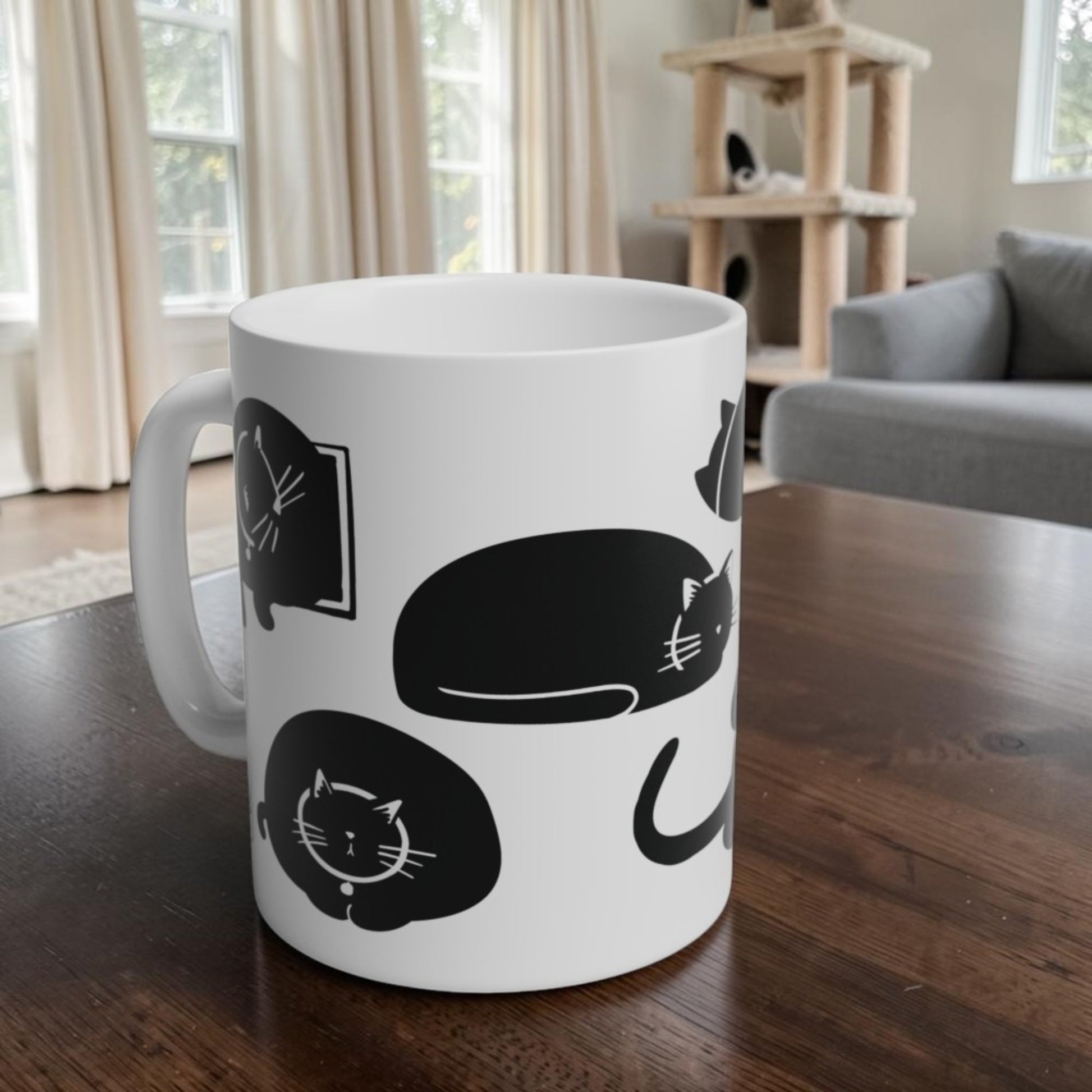 White mug with black cat illustrations on a wooden table in a living room.
