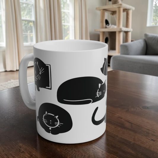 White mug with black cat illustrations on a wooden table in a living room.