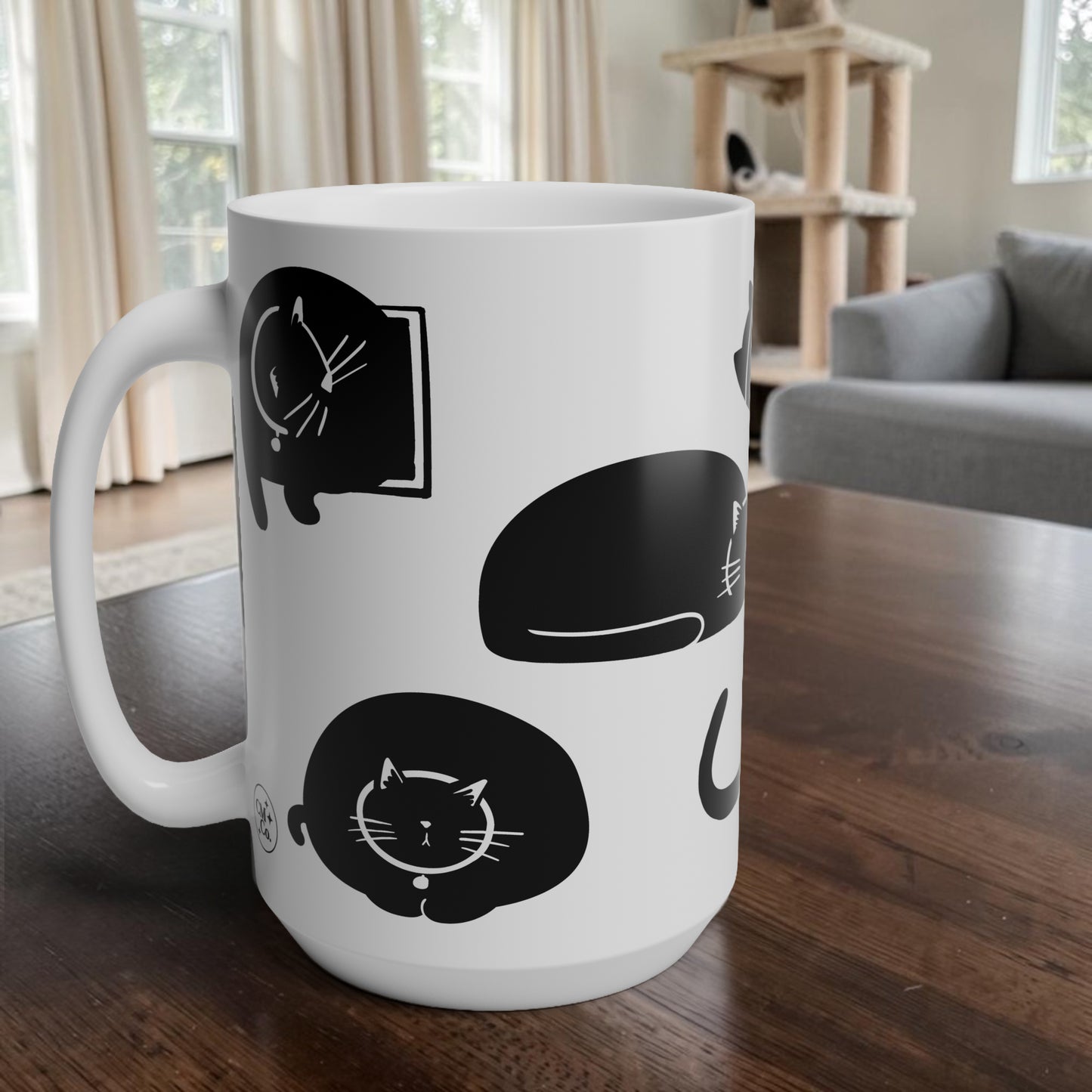 White mug with black cat illustrations on a wooden table in a living room.