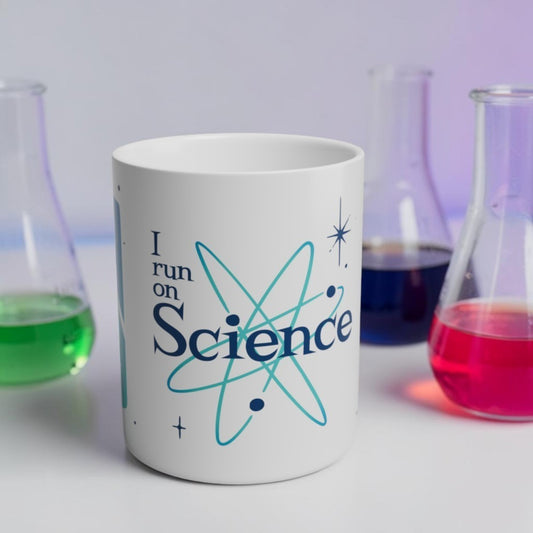 White mug with 'I run on Science' text and atom symbol, surrounded by beakers with colorful liquids.